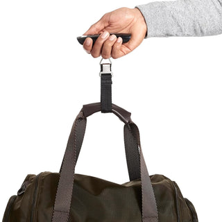Hand holding a digital scale for luggage while weighing a travel duffel bag.